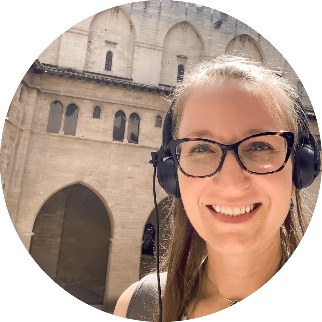 Lauren of Travelers Learn Languages with headphones on with the walls of the Pope's Palace in Avignon France in the background